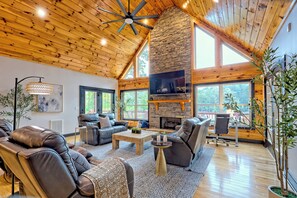 A spacious living room with leather sofas, a stone fireplace, and large windows.