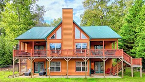 A large, two-story log cabin with a green roof, multiple balconies, and a covered front porch. - Lakefront Luxury w/ Dock + Fenced Yard (Blairsville)