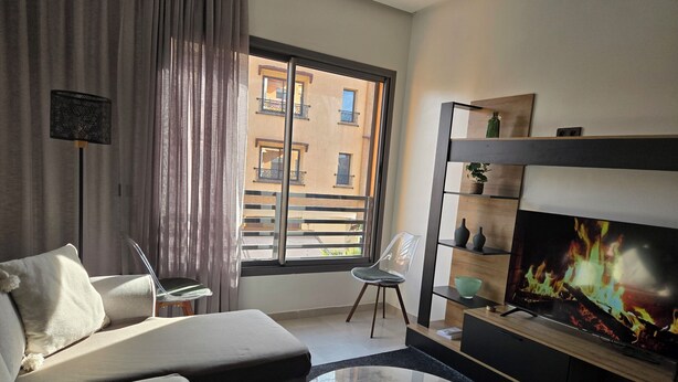 Una sala de estar moderna con un sofá, una mesa de centro, un televisor y vistas al balcón exterior.