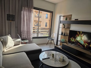 Un salon moderne avec un canapé, une table basse, un téléviseur et une vue sur le balcon extérieur.