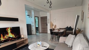 Una sala de estar moderna con un televisor de pantalla plana, un sofá, una mesa de centro y un comedor al fondo.