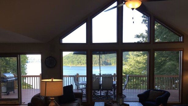 Ein großzügiges Wohnzimmer mit großen Fenstern mit Seeblick, einem Grill draußen und einer gemütlichen Sitzecke.