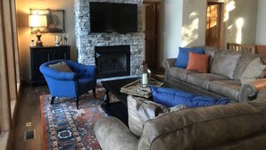 Ein Wohnzimmer mit Kamin aus Stein, einem darüber montierten Fernseher und einer Sofagarnitur.