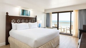 Una habitación de hotel con una cama grande, vista al océano y un balcón con sillas.