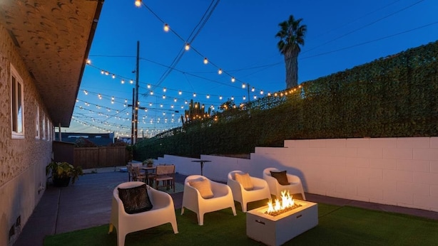 Eine Terrasse im Freien mit weißen Stühlen, einer Feuerstelle und Lichterketten.