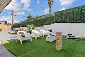 A patio area with artificial grass, white plastic chairs, a wooden bench, and a white brick wall. - Outdoor Oasis! 4BR Home w/ Projector, Games & BBQ! (San Diego)