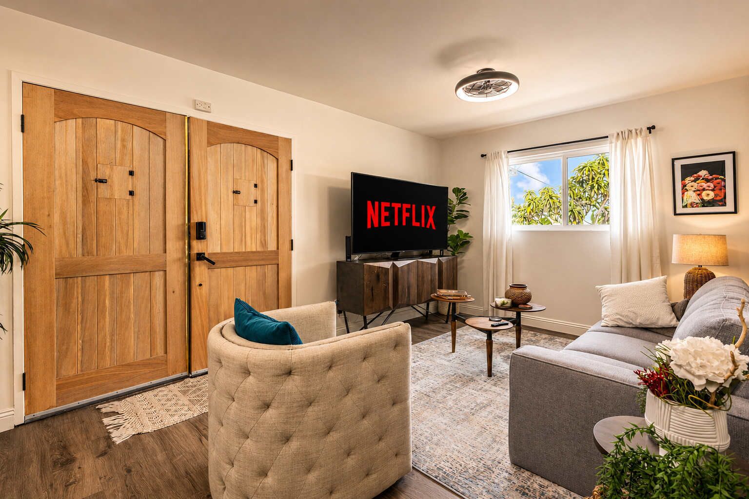 A living room with a television, a sofa, a chair, a coffee table, and a large window with curtains.