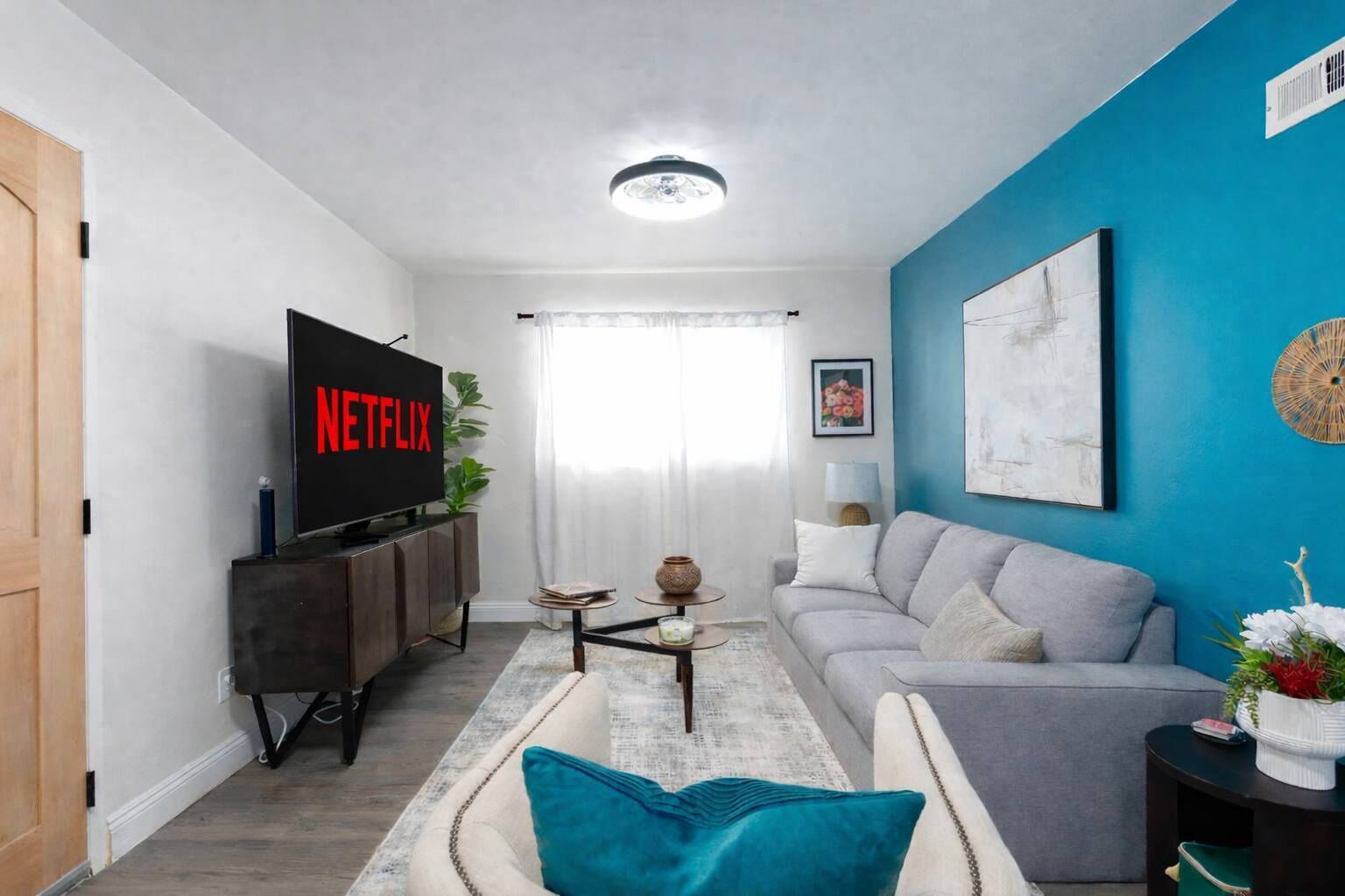 A living room with a flat-screen TV, a grey sofa, a coffee table, and a blue accent wall.