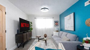 Ein Wohnzimmer mit Flachbildfernseher, grauem Sofa, Couchtisch und blauer Akzentwand.