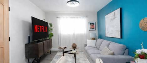 A living room with a flat-screen TV, a grey sofa, a coffee table, and a blue accent wall.