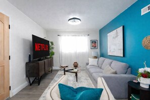 Ein Wohnzimmer mit Flachbildfernseher, grauem Sofa, Couchtisch und blauer Akzentwand.