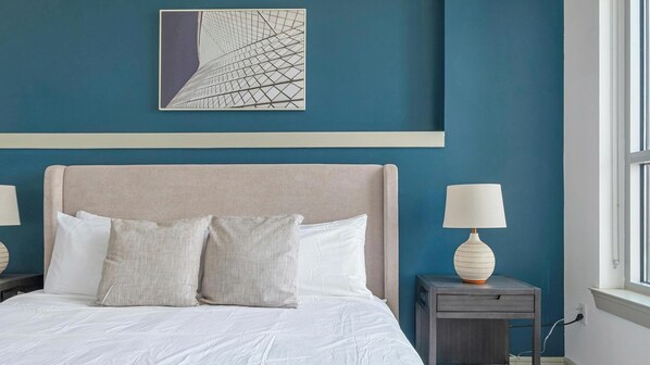 A bedroom with a bed, two bedside tables with lamps, a wall art piece, and a window. - Landing | Stunning 1BD, Gym, Pool (Houston)