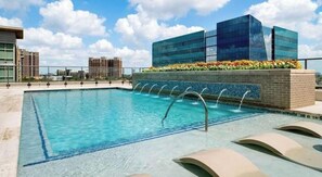 Piscina no terraço com água azul cristalina, rodeada por edifícios modernos e um céu claro.
