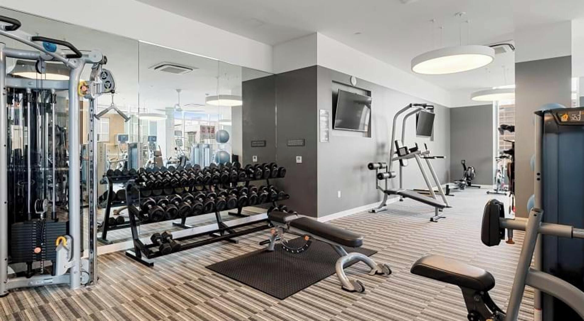 Un gimnasio con equipo de ejercicio variado, incluyendo mancuernas, una cinta de correr y máquinas de pesas.