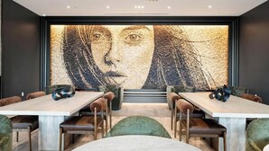 Ein moderner Essbereich mit großem abstrakten Kunstwerk an der Wand, Holztischen und grünen Sitzstühlen.