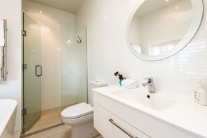 Une salle de bain moderne avec une douche à parois de verre, des toilettes blanches, un meuble-lavabo avec un miroir et un évier.