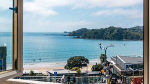Vista costeira com praia, um cais e uma colina arborizada.