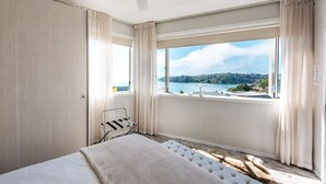 Quarto com cama, janela com vista para o mar e ventoinha no teto.