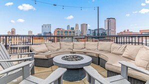 Eine Dachterrasse mit einer gebogenen Couch, einem runden Tisch mit Steinen und einer Skyline im Hintergrund.