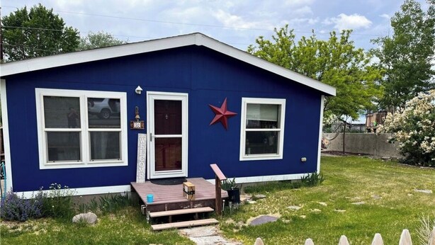 Een blauw huis met een rode ster op de muur, een houten terras en een pad van stenen dat naar de deur leidt.