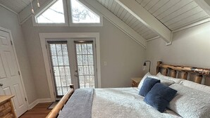 Un dormitorio con estructura de cama de madera, un ventanal con persianas y un ventilador de techo.