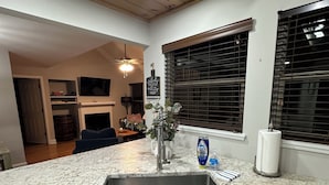 Una cocina con encimera de granito, armarios blancos, pileta de acero inoxidable y ventilador de techo.