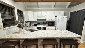 Una cocina con una isla central, armarios blancos, microondas, refrigerador y pileta.