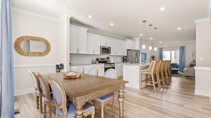 Una cocina moderna con armarios blancos, electrodomésticos de acero inoxidable y una mesa de comedor de madera con sillas.