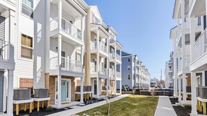 Una hilera de edificios de apartamentos modernos de varios pisos, con balcones, una mediana verde y unidades de aire acondicionado exteriores.