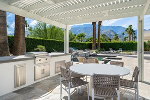An outdoor patio with a grill, dining table, and chairs, overlooking a pool and mountains. -   Casa del Sol Saltwater Pool, Fire Pit, Espresso Bar Uniquely Designed Bedrooms (Palm Springs)