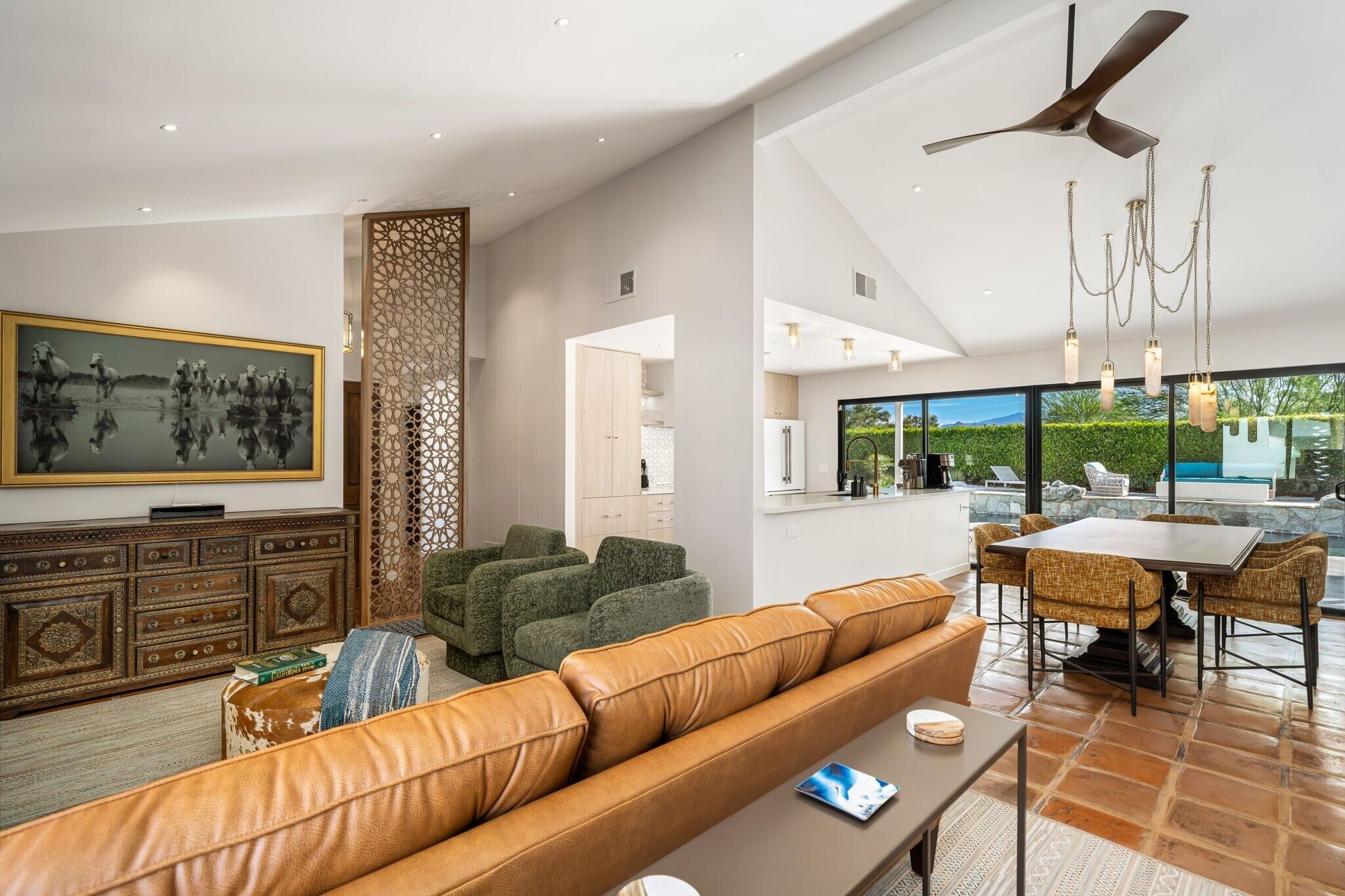 Un salon moderne avec un canapé en cuir, un coin repas avec des chaises, un ventilateur de plafond et un grand téléviseur.