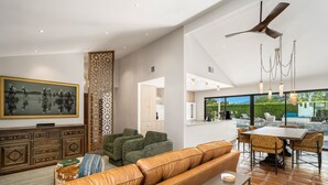 Ein modernes Wohnzimmer mit einer Ledersofa, einem Essbereich mit Stühlen, einem Deckenventilator und einem großen Fernseher.