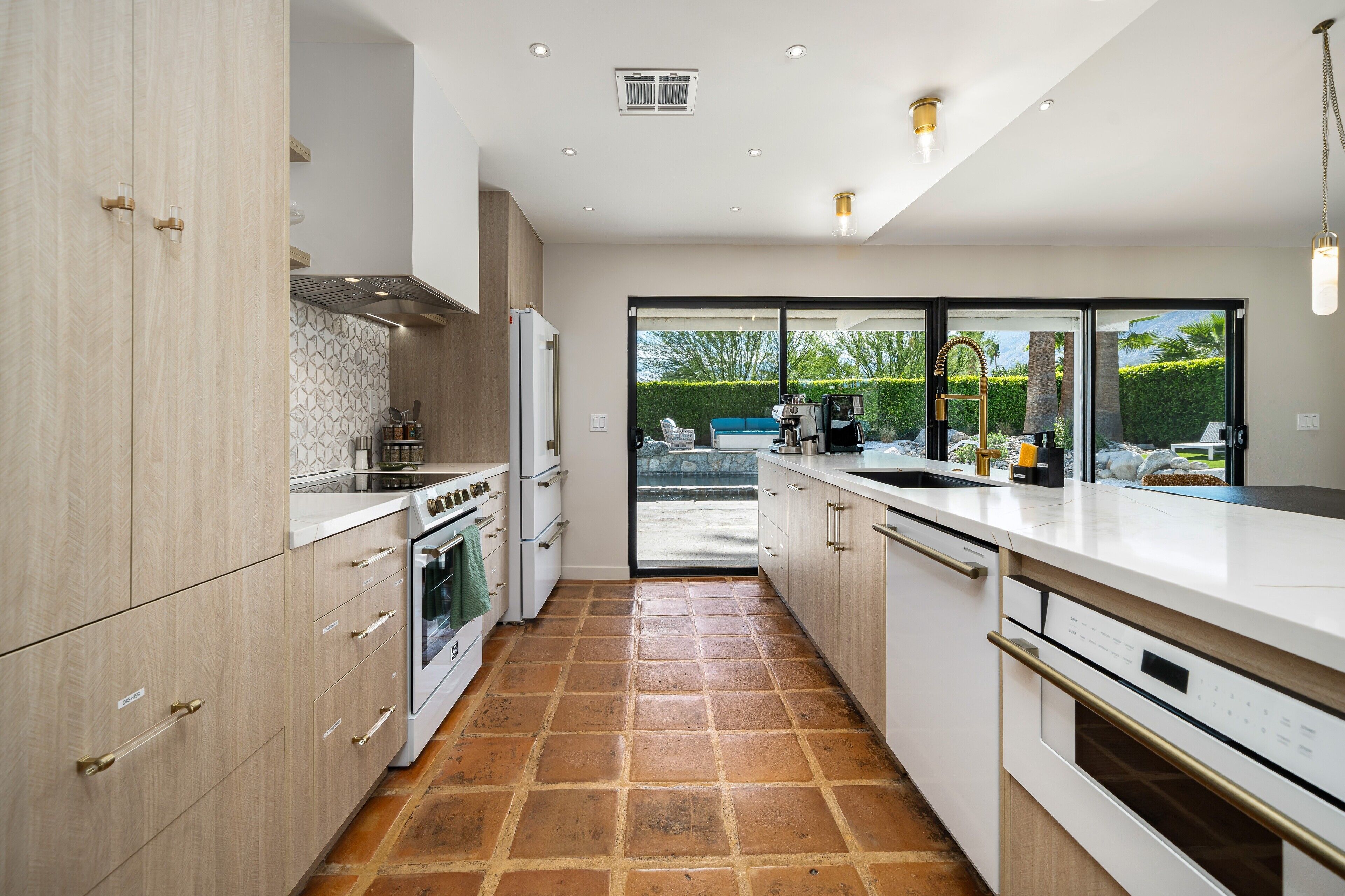 Une cuisine moderne dotée d’un grand îlot central, d’un four encastré et donnant sur un espace extérieur grâce à des portes vitrées.