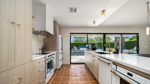 Eine moderne Küche mit einer großen Kochinsel, einem eingebauten Backofen und Blick durch Glastüren in einen Außenbereich.