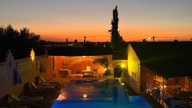 En swimmingpool med udsigt til solnedgang, liggestole og en bygning med balkon.