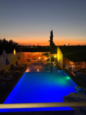 A swimming pool with a view of a sunset, lounge chairs, and a building with a balcony. - Domaine JJ – Guesthouse with pool, garden & Atlas view near Marrakech (Marrakech)