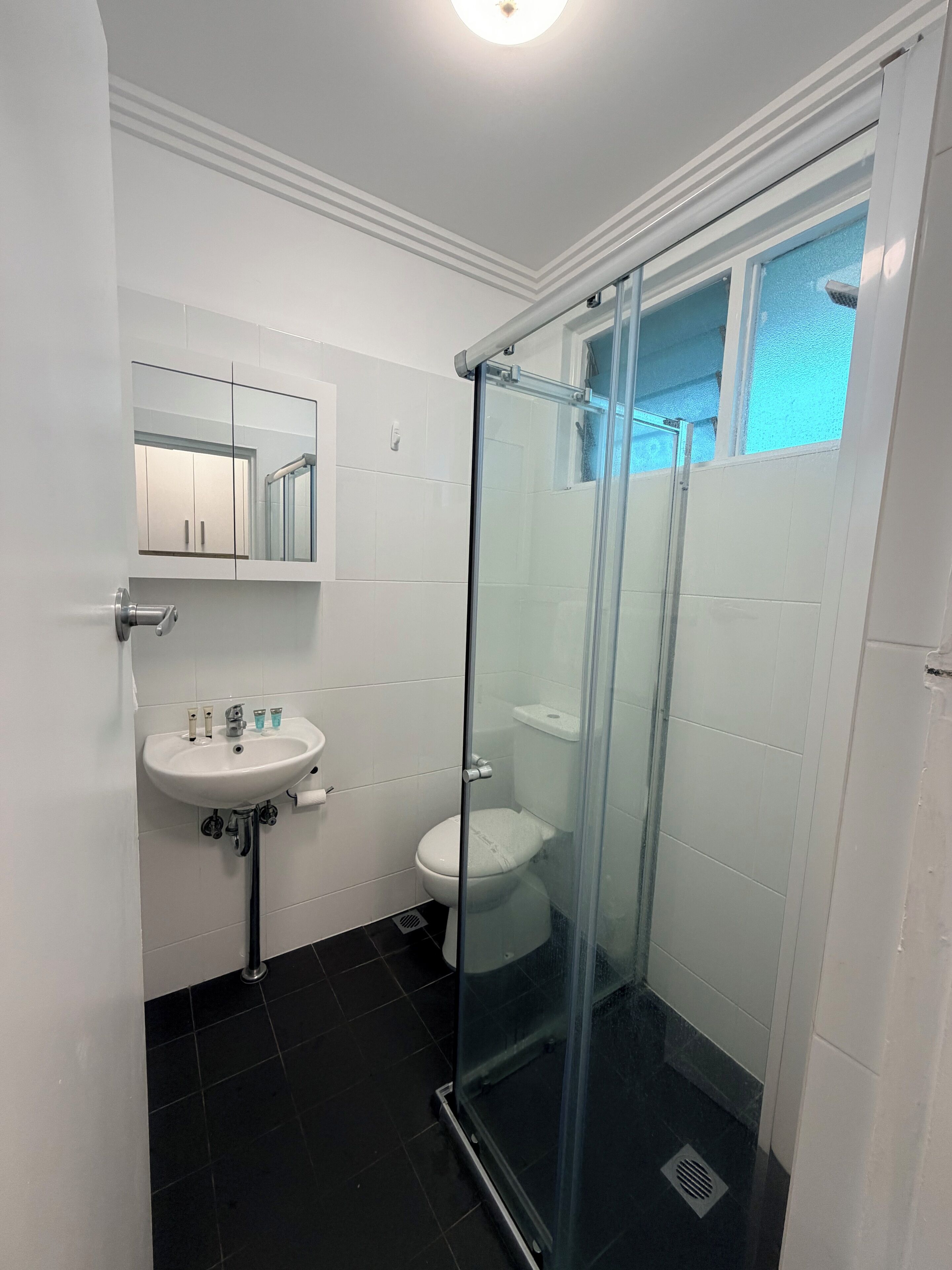 Un bagno moderno con cabina doccia in vetro, un lavandino bianco con specchio sopra e un water.