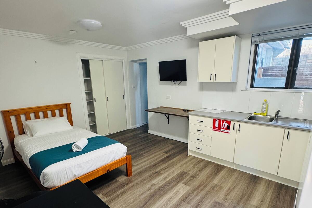 Une chambre avec un lit, un bureau, une télévision et un coin cuisine.
