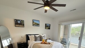 Un dormitorio con cama, mesitas de noche, ventilador de techo y un amplio ventanal con vistas.