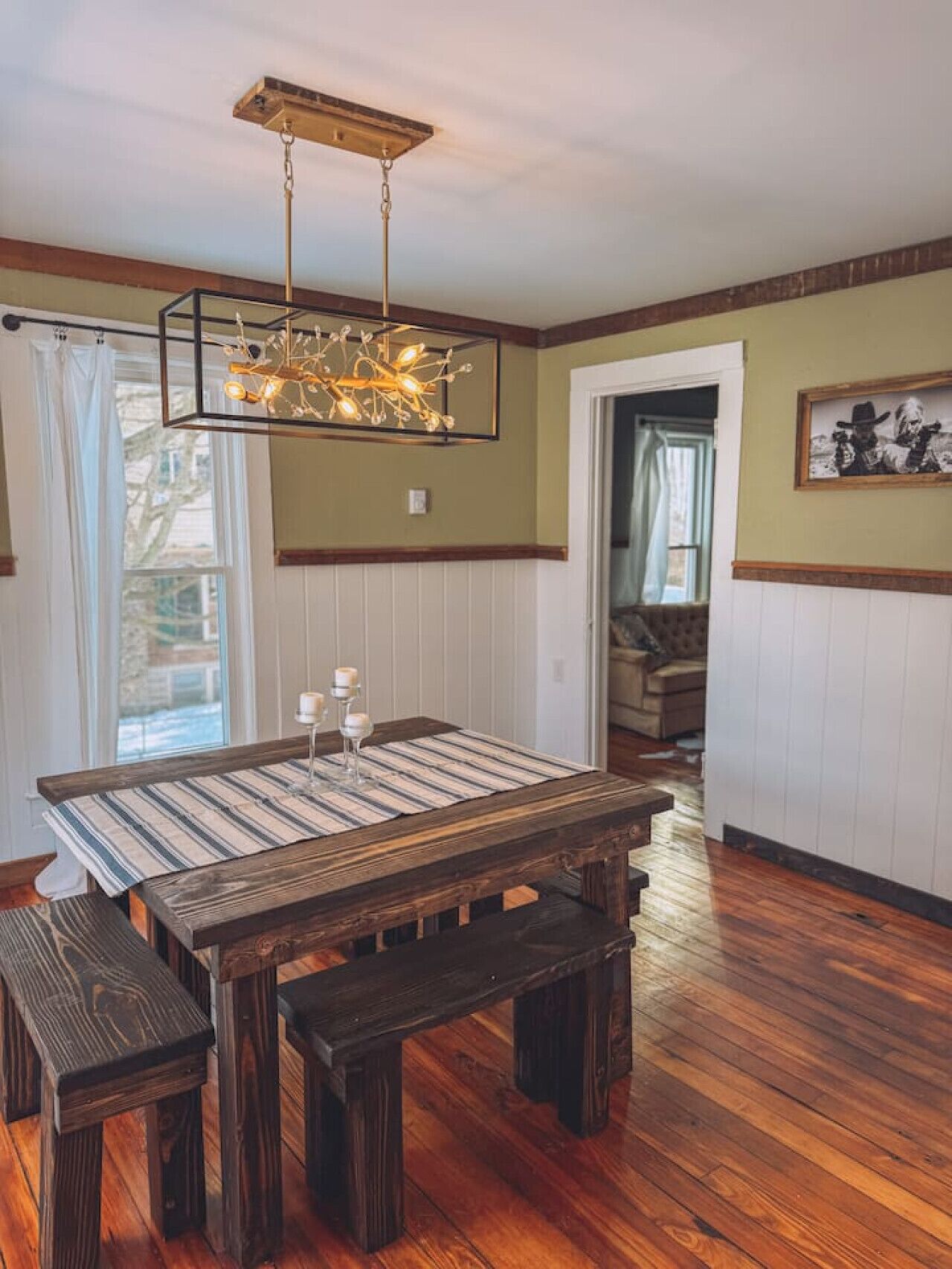 A dining area with a wooden table and benches, a hanging light fixture, and a framed picture on the wall.
