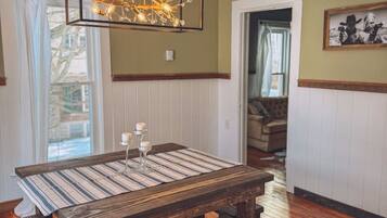A dining area with a wooden table and benches, a hanging light fixture, and a framed picture on the wall.