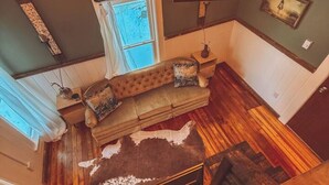 A high-ceiling room with a wooden floor, a sofa with cushions, a mounted TV, and a unique chandelier. - Gangsters Paradise @ Renegade Hideaways (Niles)