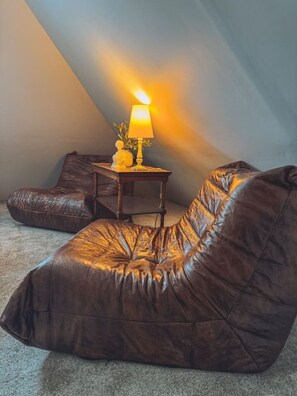 Een kamer met een bruine leren relaxfauteuil, een klein houten bijzettafeltje met een lamp en een potplant.