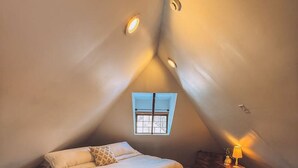 A bedroom with a bed, a small window, a wooden bench, and a lamp. - Gangsters Paradise @ Renegade Hideaways (Niles)