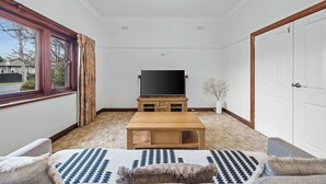 A room with a television on a wooden stand, a window with curtains, a door, and a patterned rug. - Charming Cozy Home Near Local Shops & Chadstone SC (Camberwell)