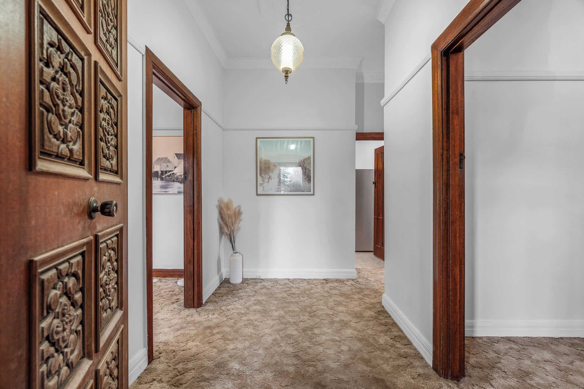 A hallway with wooden doors, a hanging light fixture, a framed picture on the wall, and a carpeted floor.