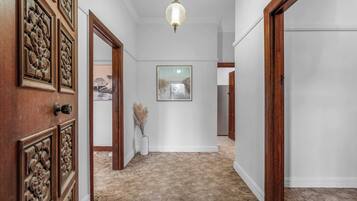 A hallway with wooden doors, a hanging light fixture, a framed picture on the wall, and a carpeted floor.