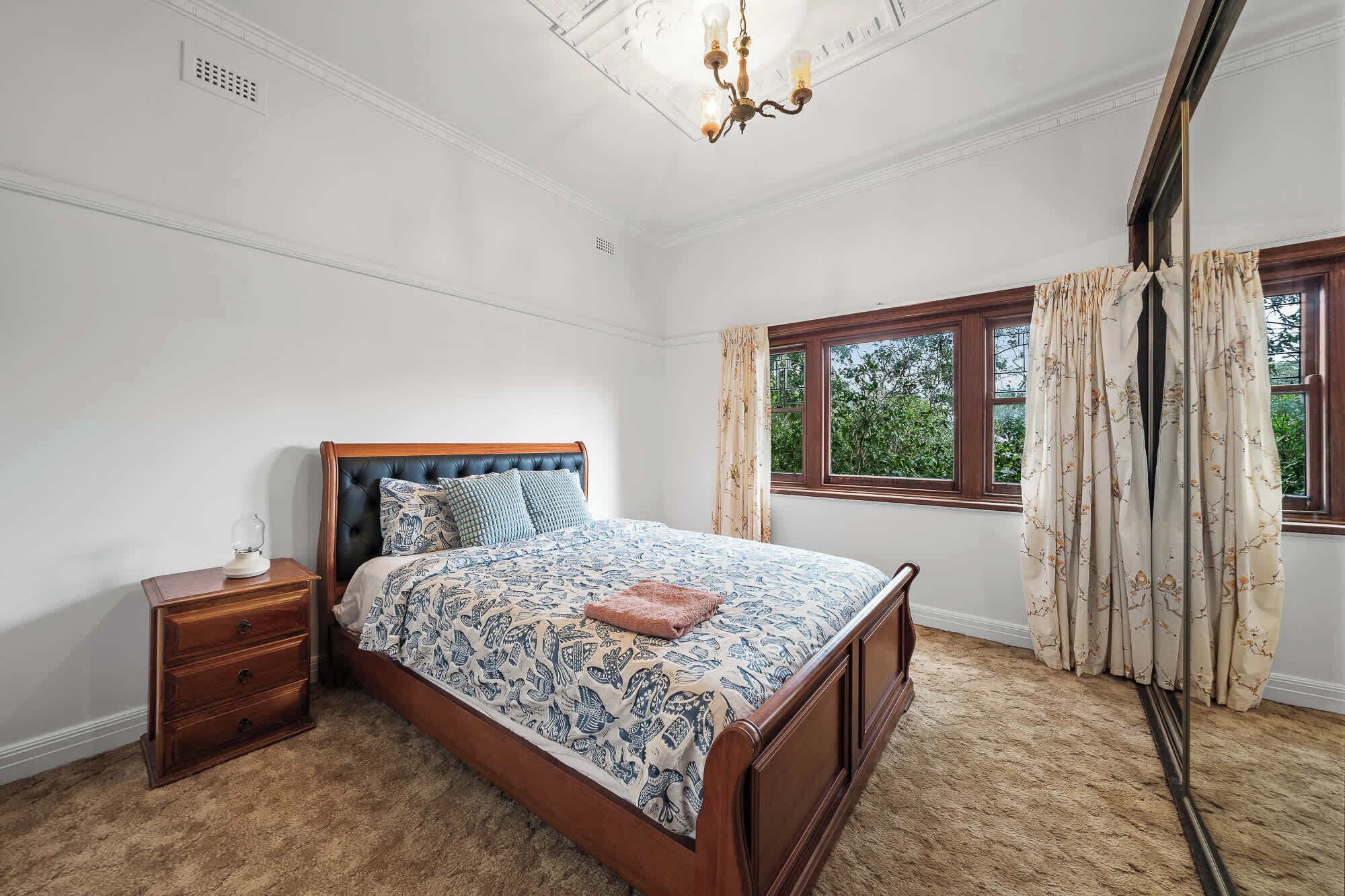 A bedroom with a bed, a nightstand, a window with curtains, and a chandelier.