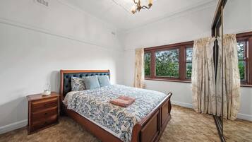A bedroom with a bed, a nightstand, a window with curtains, and a chandelier.