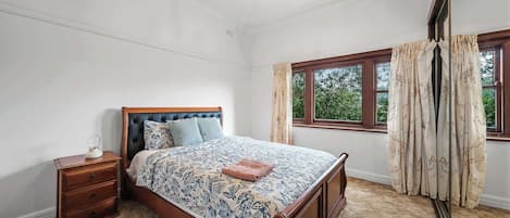 Une chambre à coucher avec un lit, une table de chevet, une fenêtre avec des rideaux et un lustre.